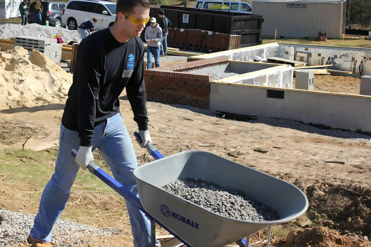 A man pushing a wheelbarrow of gravel past a new house foundation
